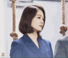 a woman in a blue suit stands in front of ropes hanging from a wall