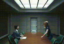 a man and a woman are sitting at a conference table in a dark room