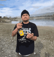 a man wearing a black t-shirt that says raiders is standing in front of a lake