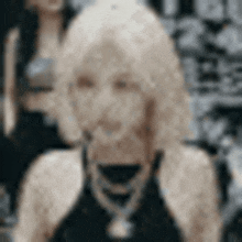 a woman with blonde hair is wearing a black tank top and necklace .