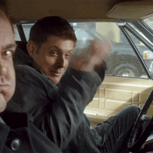 two men are sitting in a car and one is making a funny face