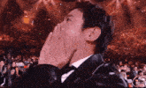 a man in a tuxedo covering his mouth with his hands