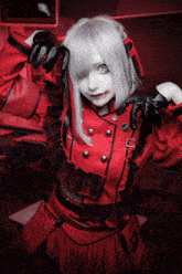 a woman with white hair and black gloves is wearing a red jacket and black skirt
