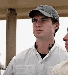 a man wearing a hat and a white shirt is standing next to another man in a white shirt .