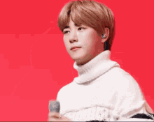 a young man is singing into a microphone while wearing a white sweater and earphones .