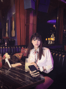 a woman sits at a table with a drink and her phone