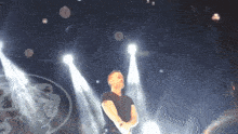 a man in a black shirt stands on a stage in front of a logo for a band
