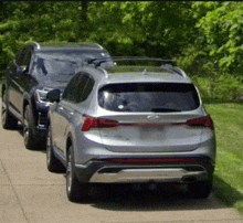 a silver suv is parked next to a black suv on a sidewalk