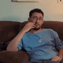 a man wearing glasses and a blue shirt with a flower on it is sitting on a couch