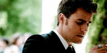 a man in a suit and tie is smoking a cigarette and looking down .