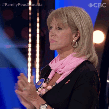 a woman wearing a pink scarf applauds during a family feud game show