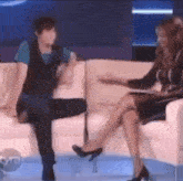 a man is sitting on a couch talking to a woman who is sitting on a chair with her legs crossed