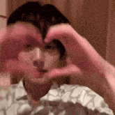 a young man is making a heart with his hands .