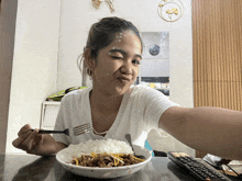 a woman sitting at a table eating a bowl of food with a fork