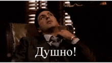 a man in a suit and tie is sitting in a chair with the words " душно " on the bottom right