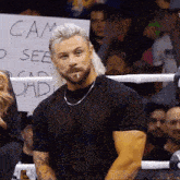 a man stands in a boxing ring holding a sign that says cam