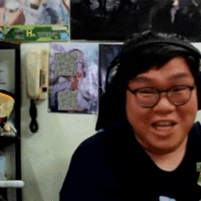 a man wearing headphones and glasses is smiling in front of a wall that has a poster that says ' happiness '