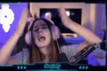 a woman wearing pink cat ears and headphones is sitting in front of a microphone and making a funny face .