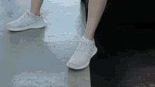 a person wearing white adidas shoes on a concrete surface