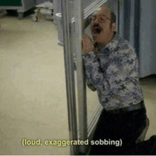 a man is peeking out from behind a door in a hospital room while talking on a cell phone .