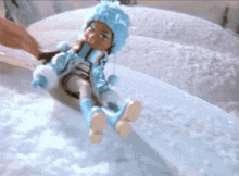 a doll wearing a blue hat and blue boots is sitting on a snowy hill .