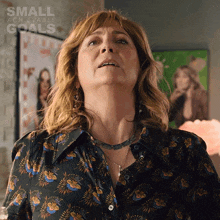 a woman in a floral shirt is looking up with a small achievable goals advertisement behind her