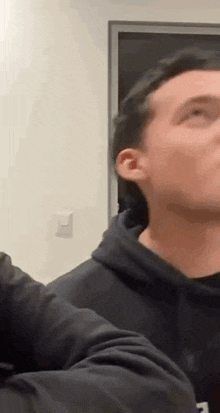 a man in a black hoodie is standing next to another man in a room and looking up .