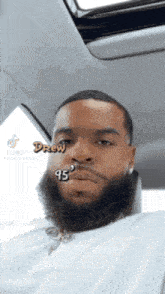 a man with a beard is sitting in a car with the name drew written on his face