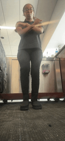 a woman wearing glasses stands with her arms crossed in front of a sink