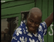 a bald man wearing a blue and white floral shirt is standing in front of a green door .