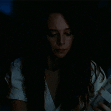 a woman with long hair and a white shirt is looking at the camera in the dark