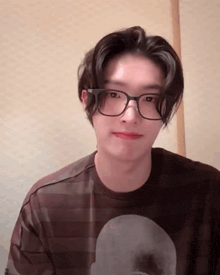 a young man wearing glasses and a t-shirt is looking at the camera .