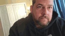 a man with a beard is wearing a black hoodie with a white logo on it