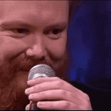 a man with a beard is holding a microphone in front of his mouth .