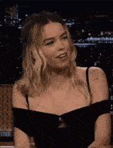 a woman in a black dress is sitting at a table talking to someone .