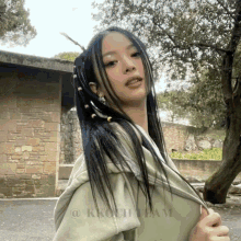 a woman with dreadlocks is standing in front of a stone wall and trees