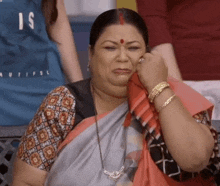 a woman in a gray and red saree is crying with her hand on her face .