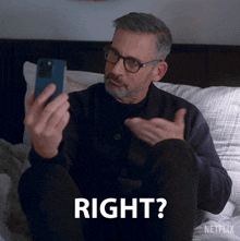 a man is sitting on a bed looking at a cell phone and says right ?