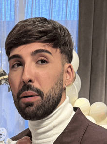 a man with a beard wearing a white turtleneck and a brown suit