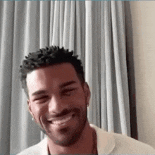 a man with a beard is smiling in front of a curtain .