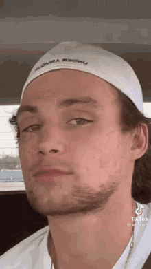 a man with a beard wearing a white hat and a white shirt .