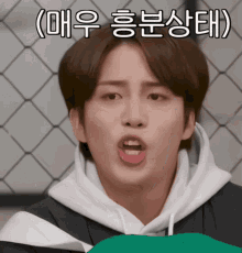 a young man making a funny face in front of a chain link fence with korean writing on it