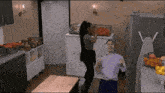 a man and a woman are dancing in a kitchen with vegetables in the background