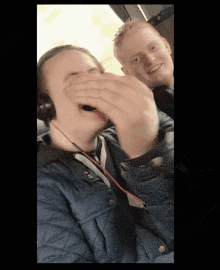 a man wearing headphones is covering his mouth while another man smiles behind him