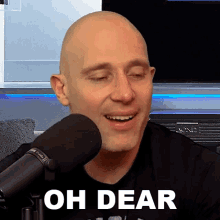 a bald man is smiling in front of a microphone with the words oh dear written below him