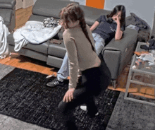 a woman is dancing in a living room while another woman sits on a couch in the background