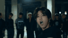a group of young men are standing in a dark room and one of them is wearing a black hoodie and earrings