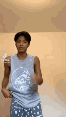a young man wearing a tank top and shorts is dancing on tiktok .
