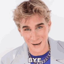 a young man is wearing a blue shirt and a silver chain around his neck and says bye
