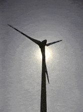 a wind turbine against a clear blue sky with the sun shining through it
